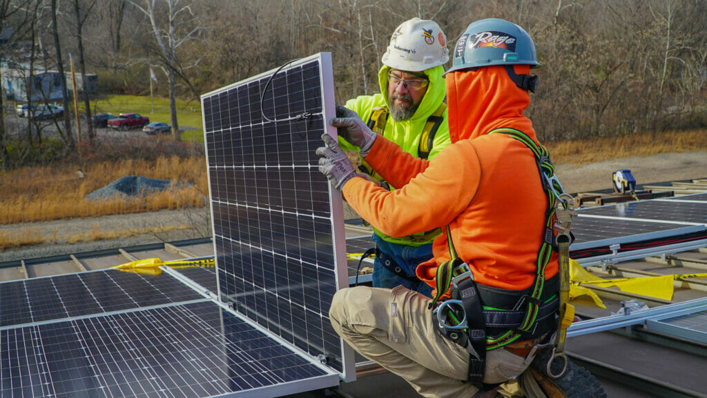 Two men on rooftop install solar panel